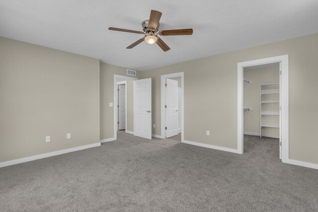 unfurnished bedroom featuring a spacious closet, baseboards, carpet floors, and visible vents