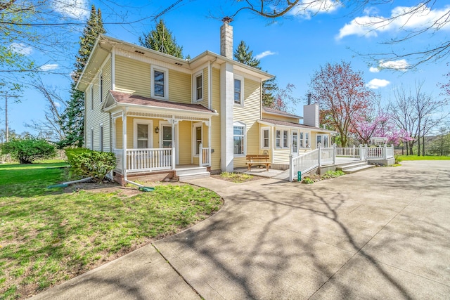 view of front facade featuring a front yard, driveway, covered porch, and a chimney