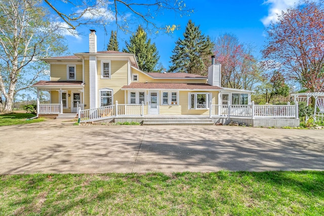 rear view of property with covered porch, a chimney, and concrete driveway