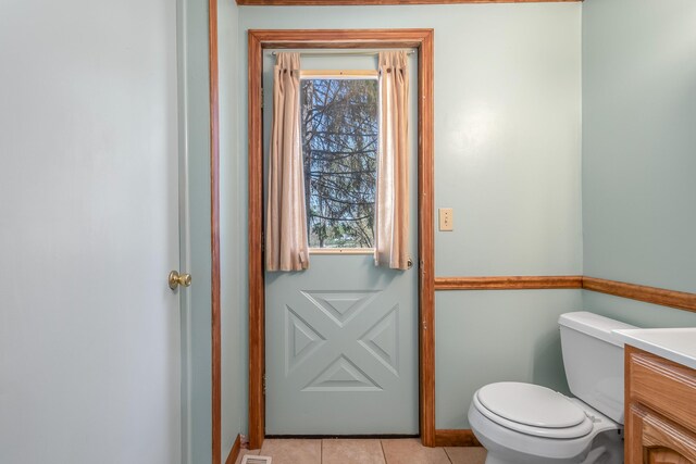 half bath with vanity, tile patterned floors, a wealth of natural light, and toilet
