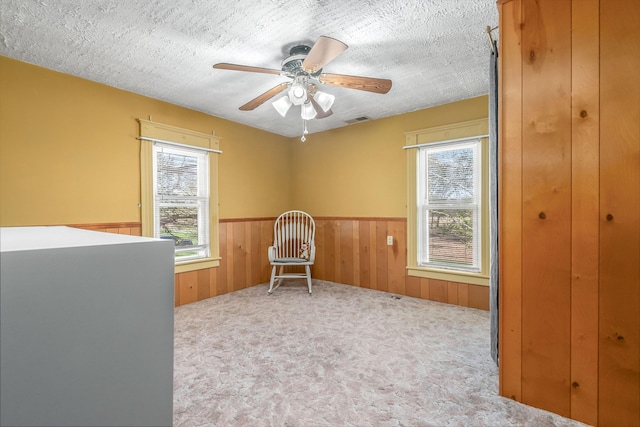 living area with visible vents, wood walls, ceiling fan, a wainscoted wall, and carpet flooring