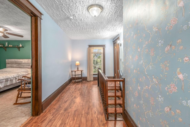 hallway with baseboards, a textured ceiling, and wood finished floors