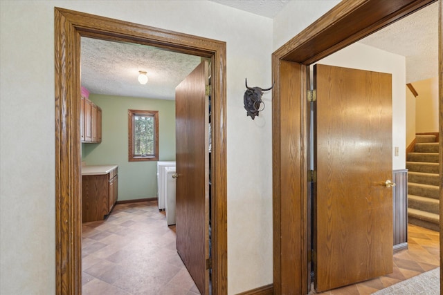 corridor with stairway, baseboards, and a textured ceiling