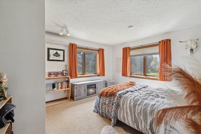 bedroom with a wall mounted air conditioner, a textured ceiling, a glass covered fireplace, and carpet flooring
