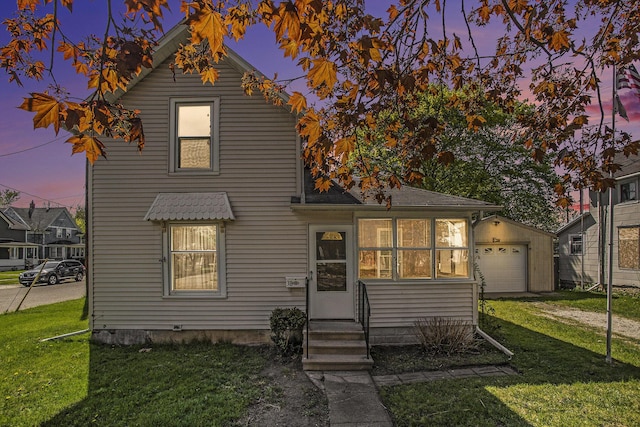 back of property at dusk featuring entry steps, a detached garage, and a lawn