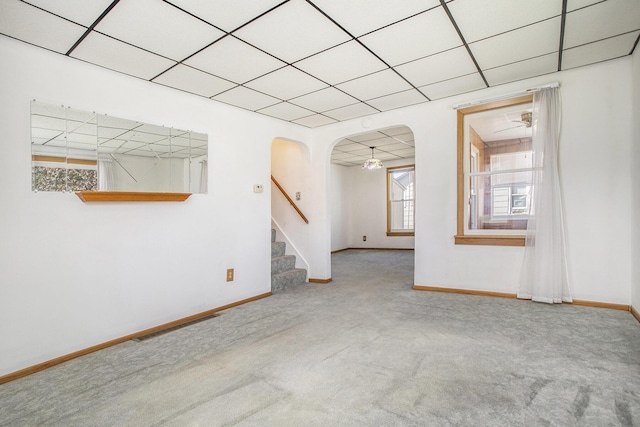 carpeted spare room featuring stairs, arched walkways, baseboards, and visible vents