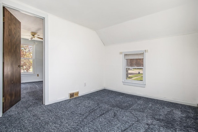 unfurnished room with ceiling fan, dark carpet, baseboards, vaulted ceiling, and visible vents