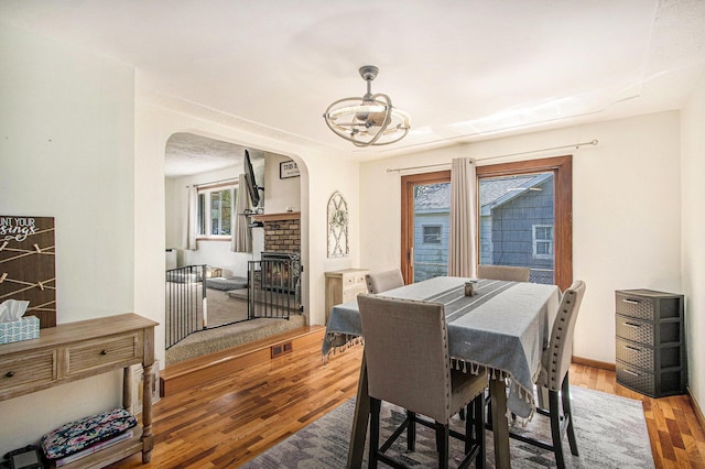 dining area featuring a fireplace, arched walkways, a chandelier, wood finished floors, and visible vents