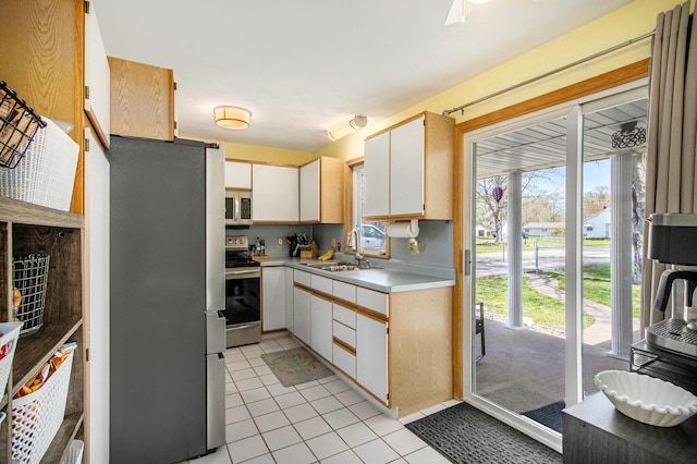 kitchen featuring appliances with stainless steel finishes, a sink, light tile patterned floors, white cabinets, and light countertops