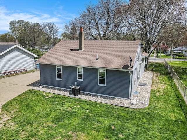 back of house with a chimney, central AC, fence, a yard, and a shingled roof