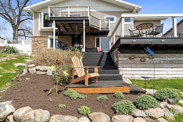 back of property with stairs, a wooden deck, brick siding, and fence