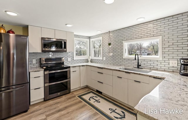 kitchen featuring decorative backsplash, appliances with stainless steel finishes, a sink, light stone counters, and light wood finished floors