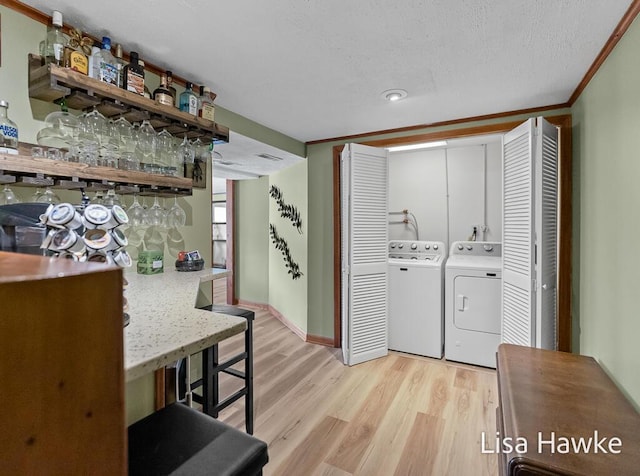 laundry room featuring laundry area, washer and dryer, light wood-style floors, a textured ceiling, and a bar