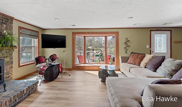 living room with a textured ceiling, ornamental molding, light wood-style flooring, and a wood stove