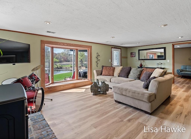living room with a textured ceiling, visible vents, crown molding, a water view, and light wood-style flooring