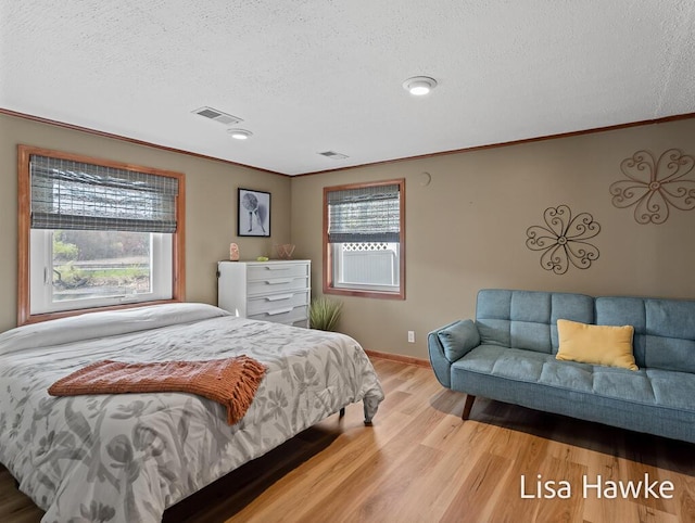 bedroom with a textured ceiling, ornamental molding, wood finished floors, and visible vents