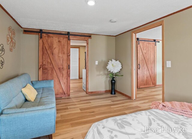 bedroom featuring baseboards, ornamental molding, light wood-type flooring, and a barn door