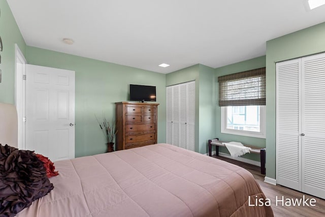 bedroom with two closets, baseboards, and wood finished floors