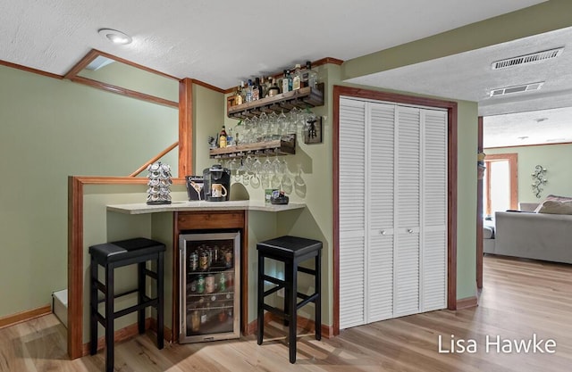 bar with a textured ceiling, a dry bar, beverage cooler, and wood finished floors