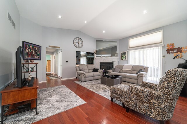 living room featuring visible vents, a glass covered fireplace, wood finished floors, baseboards, and vaulted ceiling