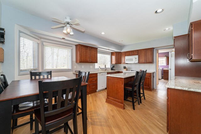 kitchen featuring light wood-type flooring, a kitchen breakfast bar, white appliances, and a center island