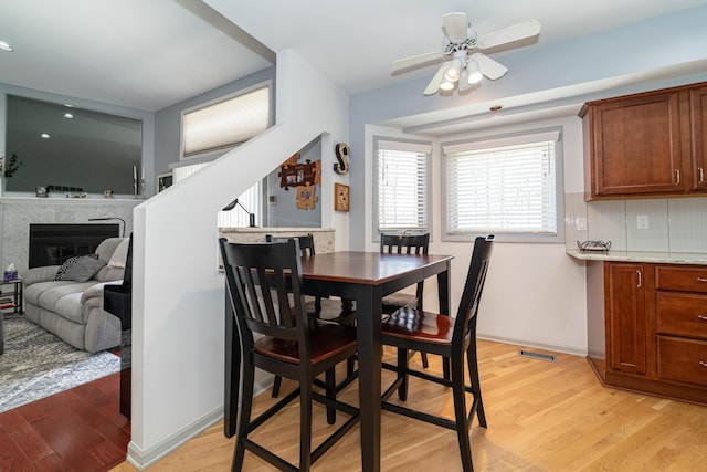 dining space with visible vents, a fireplace, light wood-style floors, baseboards, and a ceiling fan