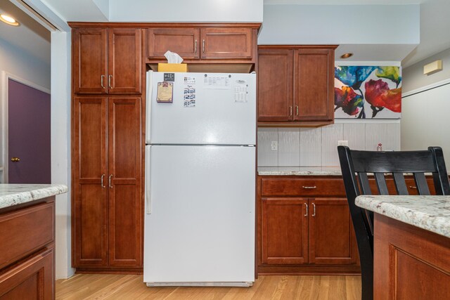 kitchen with light wood-type flooring, freestanding refrigerator, brown cabinetry, and light stone counters