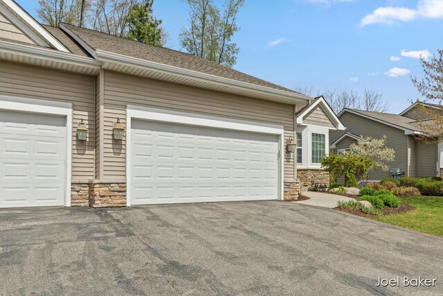 view of front of home featuring a garage, a shingled roof, stone siding, and aphalt driveway