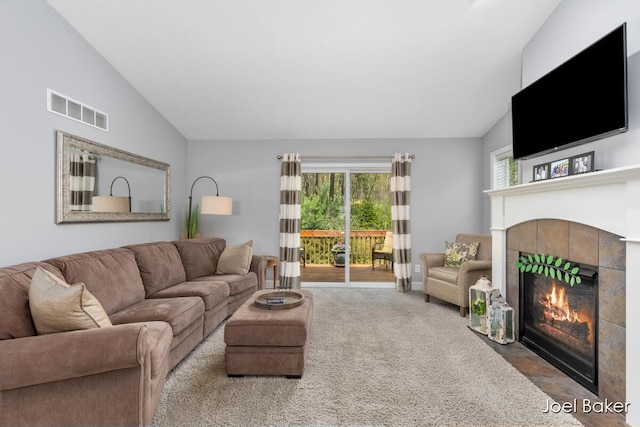 carpeted living area with visible vents, vaulted ceiling, and a tile fireplace