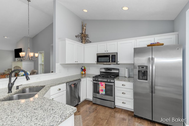 kitchen featuring light stone countertops, appliances with stainless steel finishes, an inviting chandelier, a sink, and high vaulted ceiling