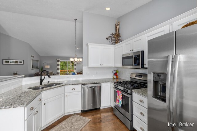 kitchen with an inviting chandelier, a peninsula, lofted ceiling, a sink, and appliances with stainless steel finishes