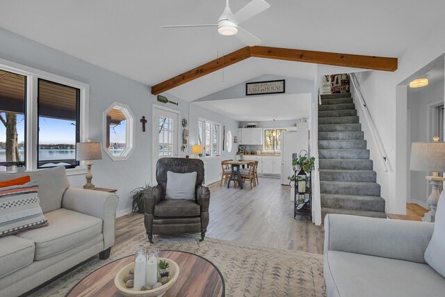 living room featuring baseboards, ceiling fan, stairway, lofted ceiling with beams, and light wood finished floors