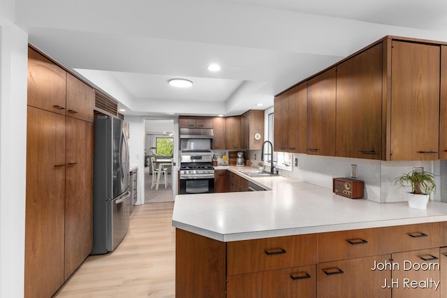 kitchen with appliances with stainless steel finishes, a sink, a raised ceiling, light countertops, and light wood finished floors