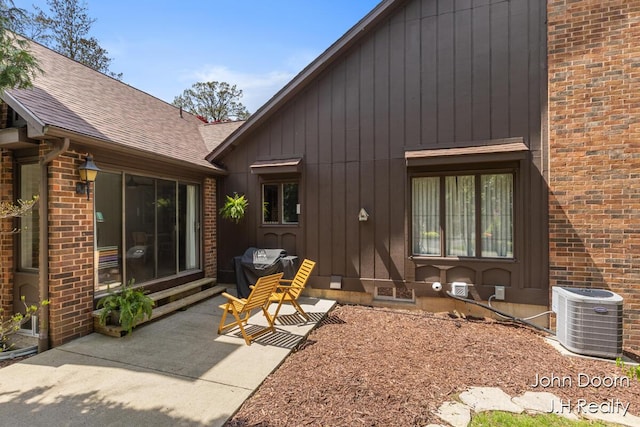 rear view of property featuring central AC unit, a patio area, board and batten siding, brick siding, and a shingled roof