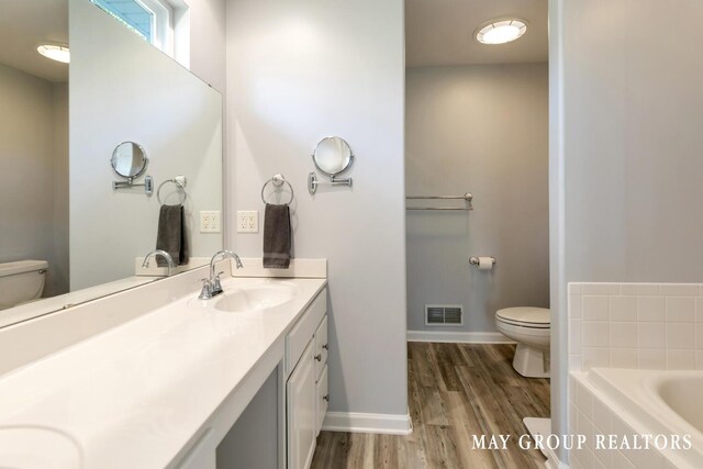 3729 Windshire Dr SE, Grand Rapids, MI 49546 - full bathroom featuring toilet, wood finished floors, double vanity, a relaxing tiled tub, and baseboards