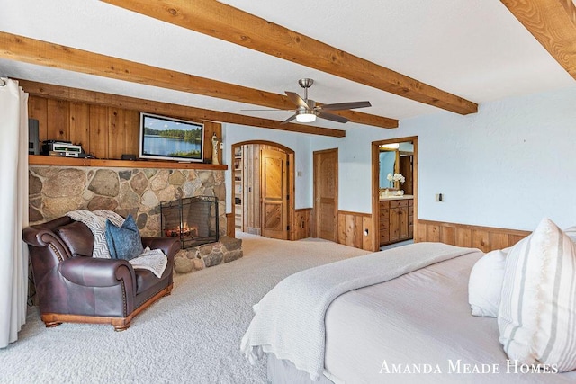 12345 92nd St SE, Alto, MI 49302 - carpeted bedroom featuring wood walls, wainscoting, beam ceiling, a stone fireplace, and arched walkways