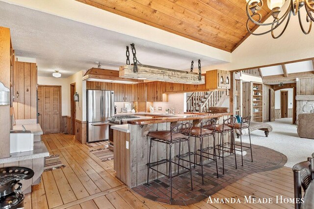 12345 92nd St SE, Alto, MI 49302 - kitchen with brown cabinets, wood walls, a peninsula, stainless steel appliances, and light wood-style flooring
