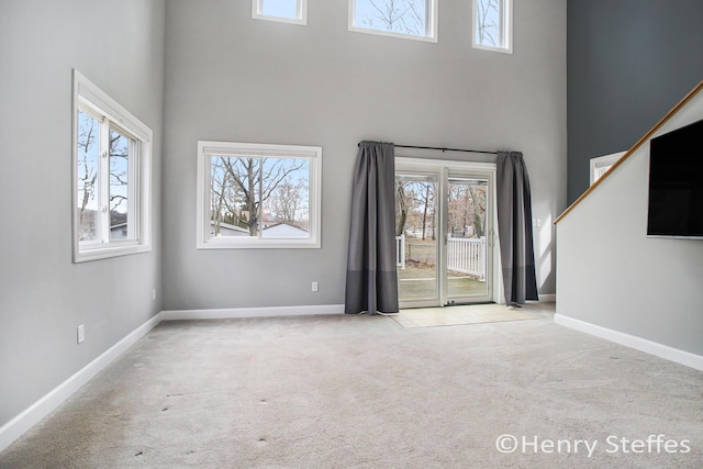 unfurnished living room with carpet floors, a towering ceiling, and a healthy amount of sunlight