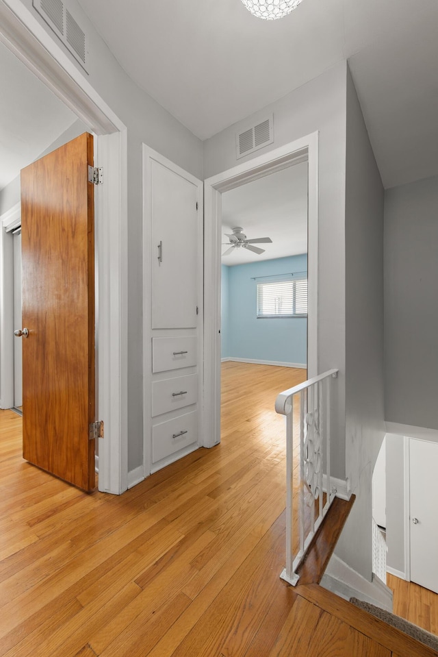 hall featuring visible vents, light wood-style floors, baseboards, and an upstairs landing