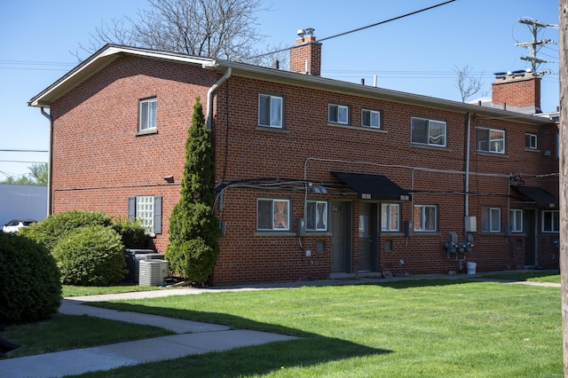 rear view of house with brick siding, a lawn, a chimney, and cooling unit