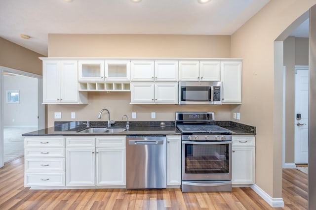 18559 Kreig Dr, Big Rapids, MI 49307 - kitchen featuring arched walkways, a sink, white cabinets, light wood-style floors, and stainless steel appliances