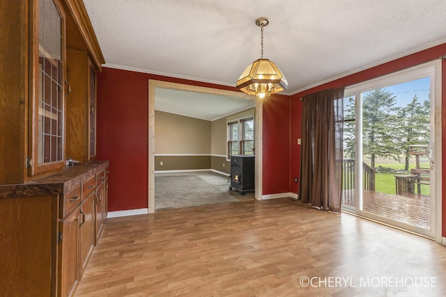 unfurnished dining area with an inviting chandelier, a wood stove, a textured ceiling, baseboards, and ornamental molding