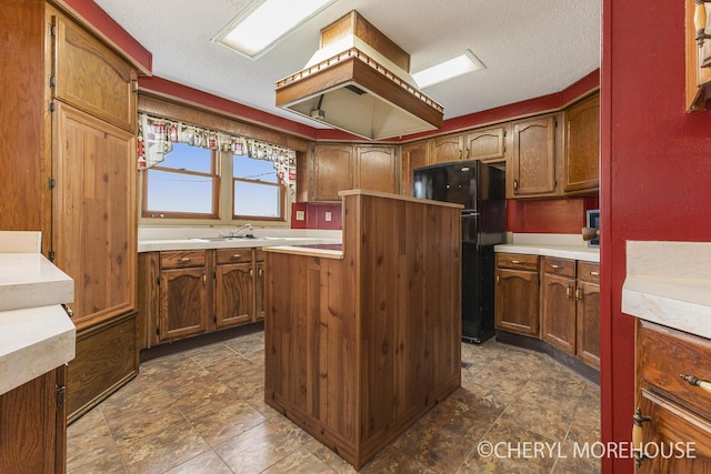 kitchen with a center island, brown cabinets, a sink, light countertops, and freestanding refrigerator