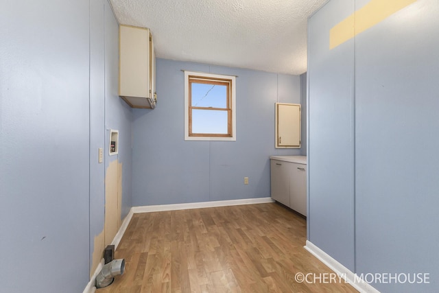 laundry room with cabinet space, a textured ceiling, baseboards, and light wood finished floors