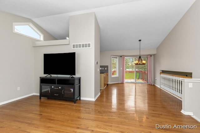 unfurnished living room featuring lofted ceiling, a chandelier, wood finished floors, and baseboards