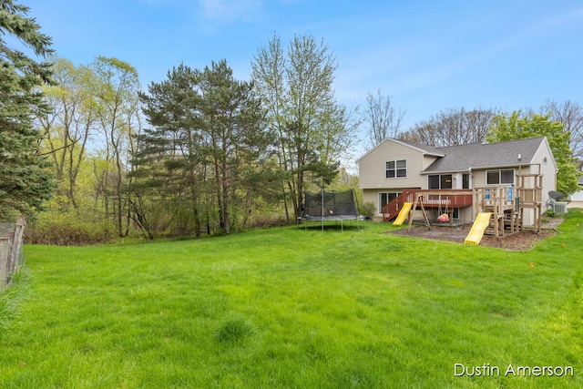 view of grassy yard with a trampoline, a wooden deck, and a playground