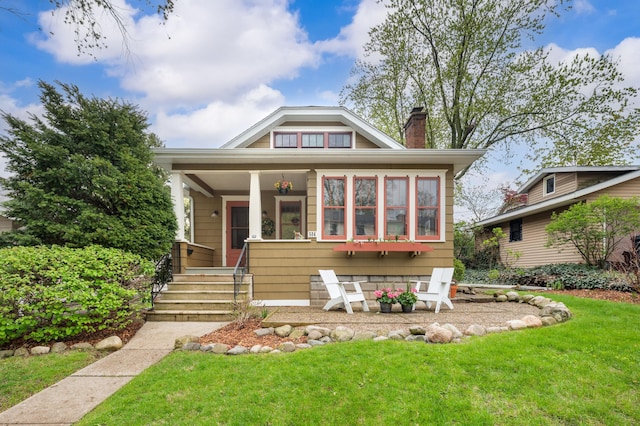 view of front facade with a chimney, a front yard, and covered porch