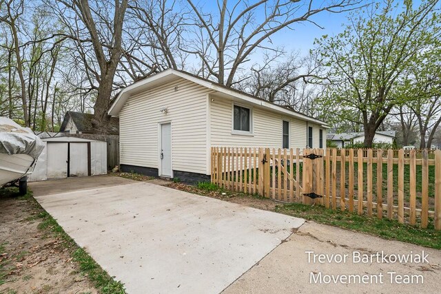 view of property exterior with a storage unit, a gate, an outdoor structure, fence private yard, and driveway