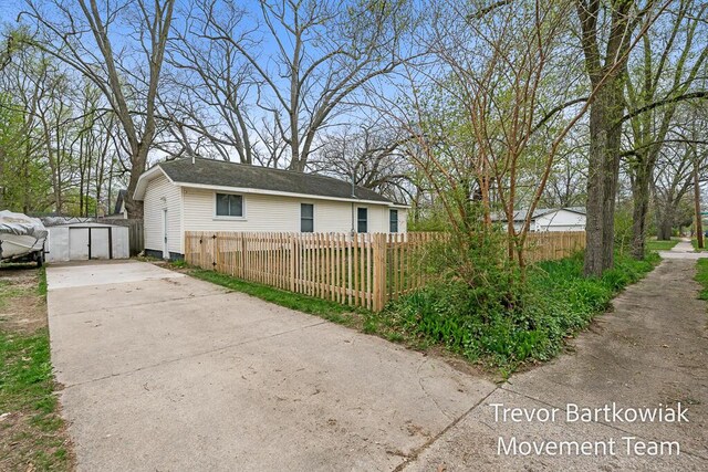 view of property exterior with concrete driveway, a fenced front yard, and a storage unit
