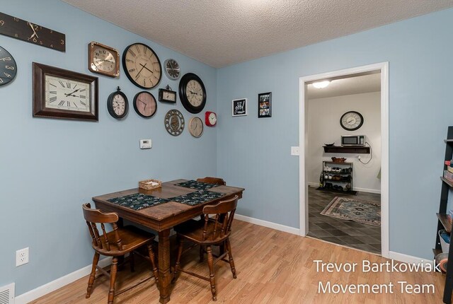 dining room featuring baseboards, a textured ceiling, wood finished floors, and visible vents